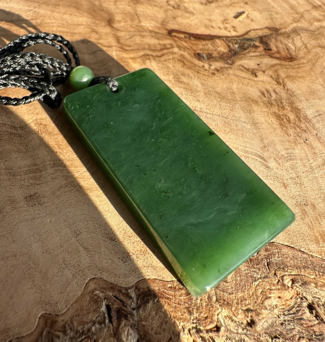 Canadian Jade Textured Rectangle Pendant 50MM with black cord and bead on a wooden surface