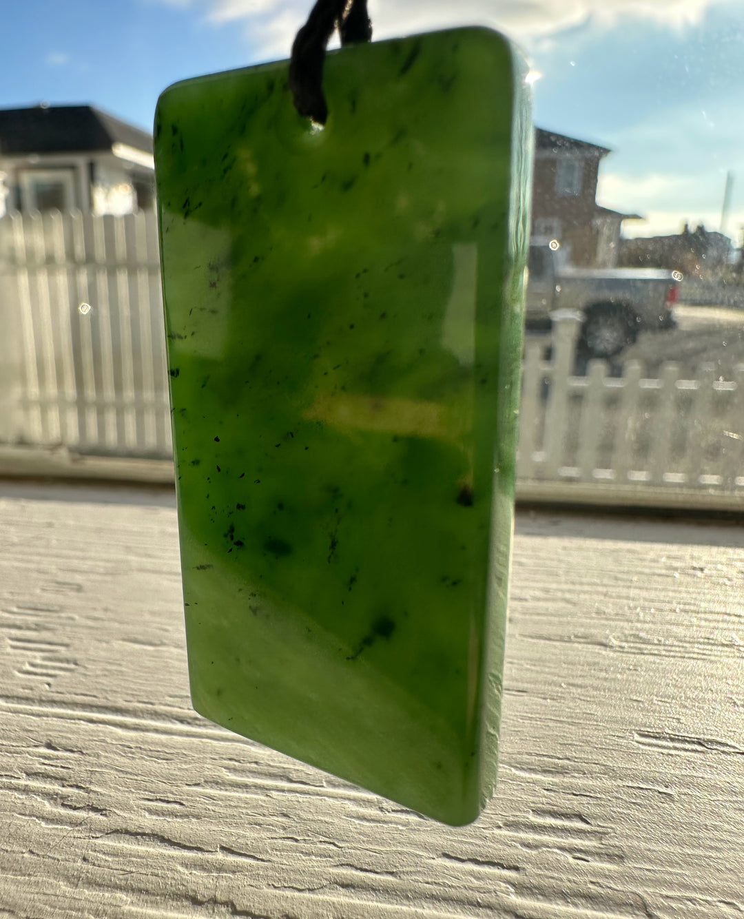 Canadian Jade Textured Rectangle Pendant 50MM suspended from a cord against a sunny window backdrop