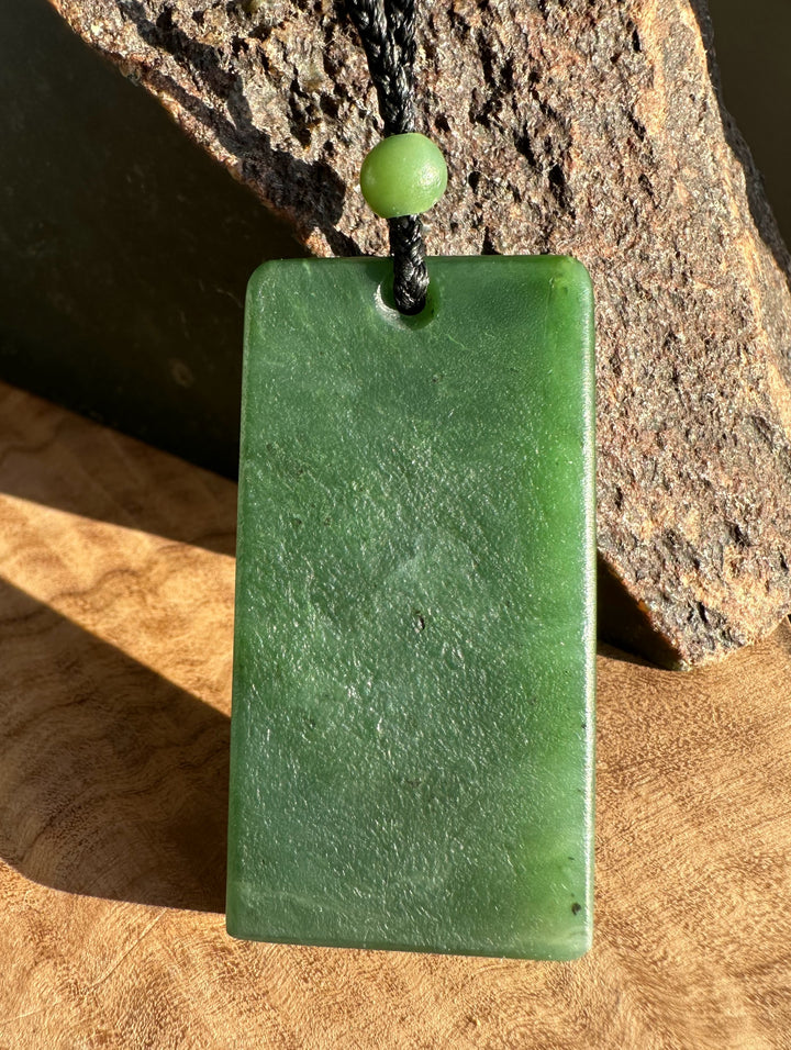 Textured rectangle jade pendant on black cord with a small green bead
