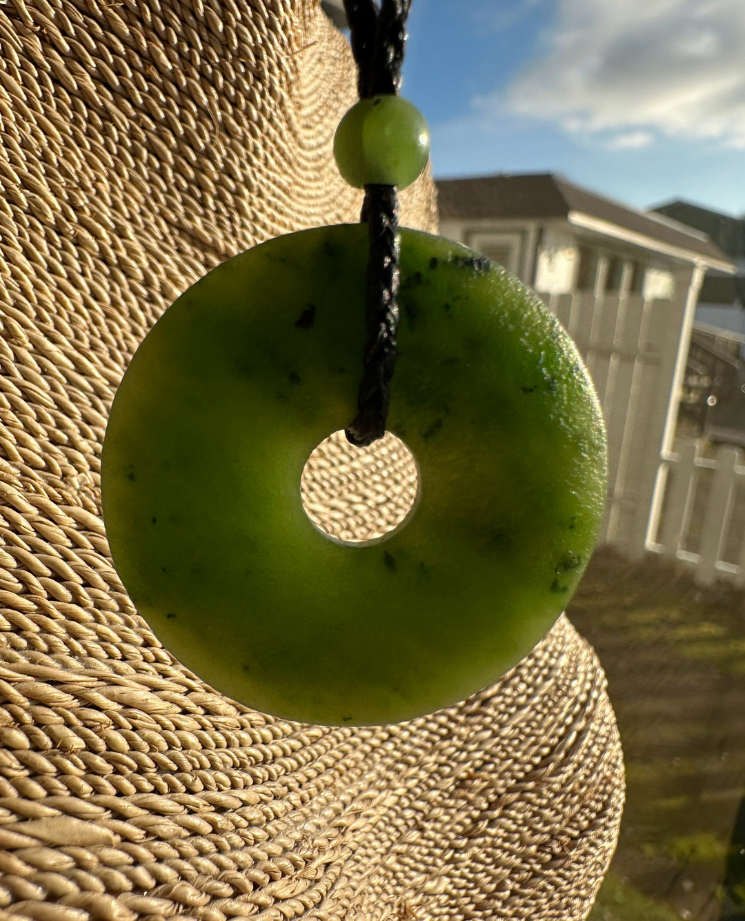Canadian jade textured donut pendant with a central hole on a braided black cord and a small green bead.