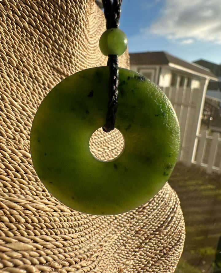 Canadian jade textured donut pendant with a central hole on a braided black cord and a small green bead.