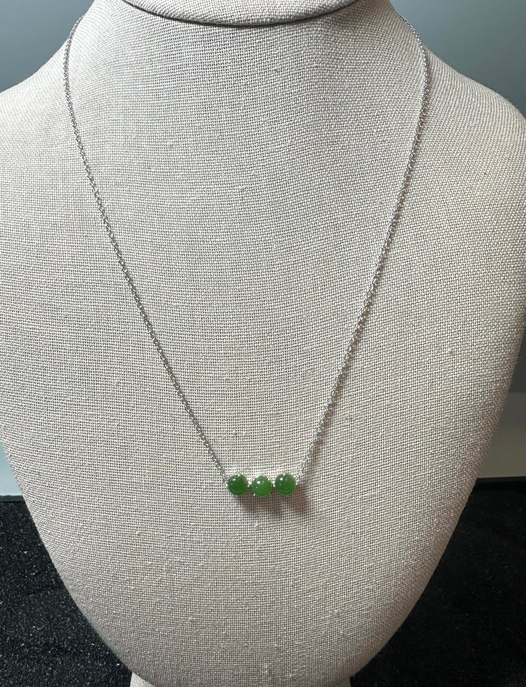 Three green jade beads on a silver chain necklace displayed on a mannequin bust.