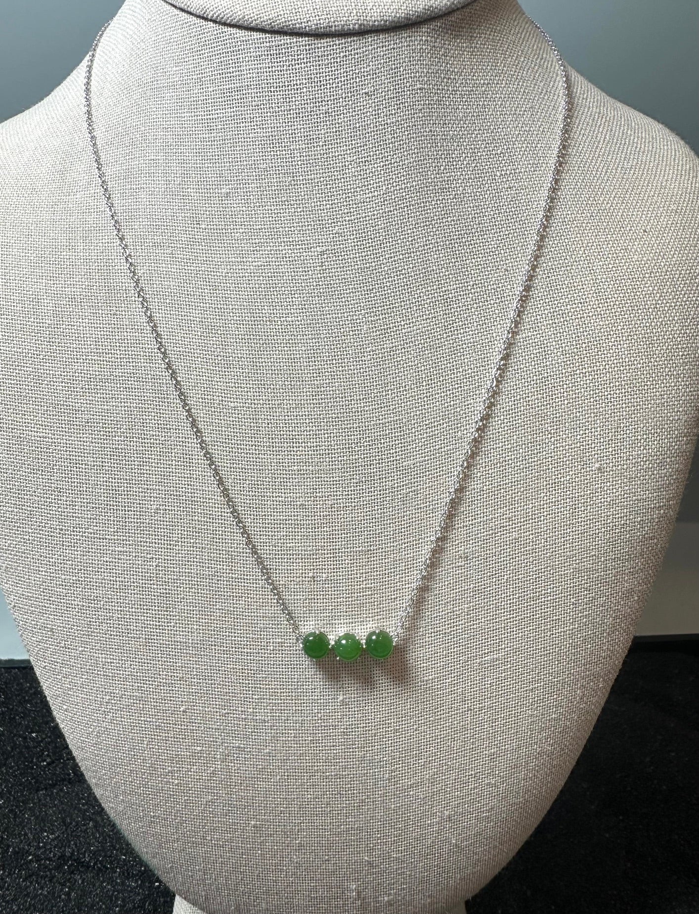 Three green jade beads on a silver chain necklace displayed on a mannequin bust.