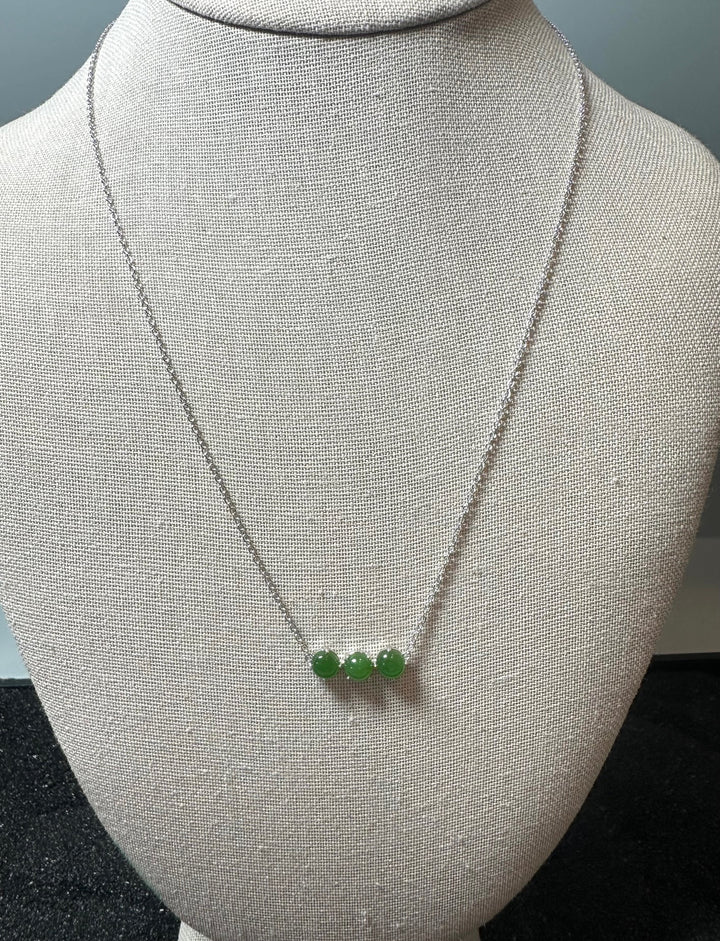 Three green jade beads on a silver chain necklace displayed on a mannequin bust.
