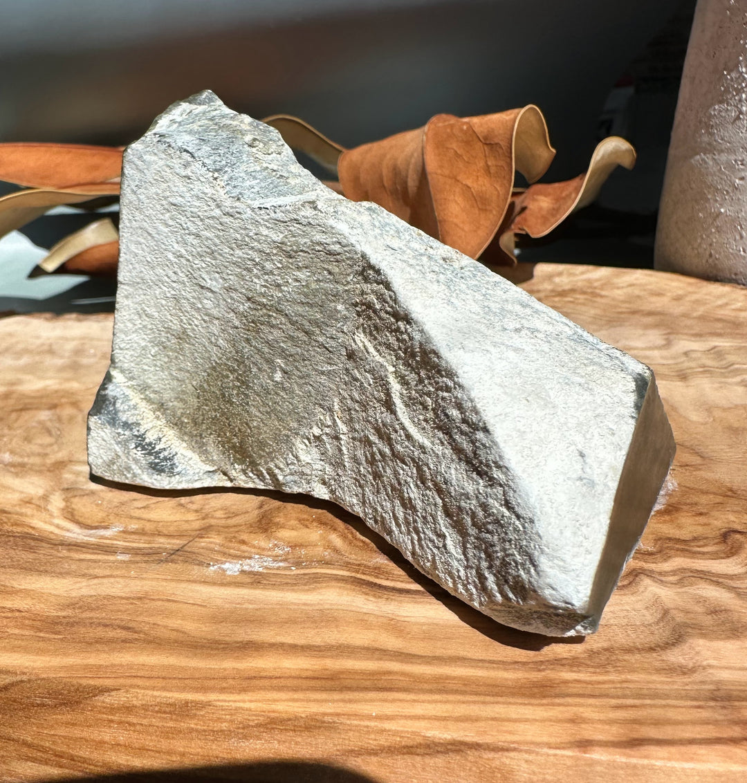 Rough gray Wyoming Honey Olive Jade stone specimen on a wooden table.