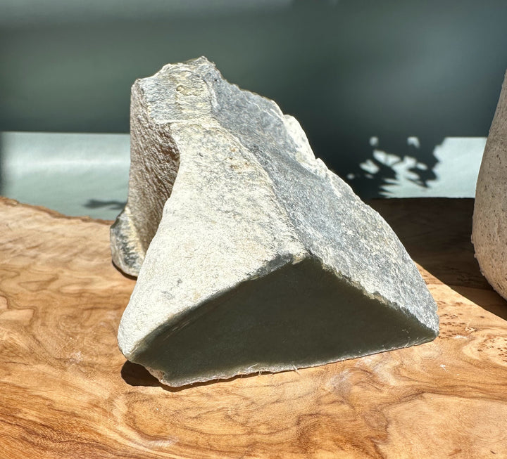 Angular Wyoming Honey Olive Jade rock on a wooden surface viewed from the side.