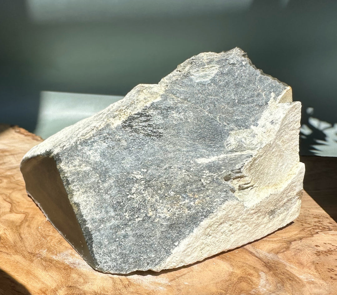 Rough Wyoming Honey Olive Jade chunk with a gray surface on a wooden table