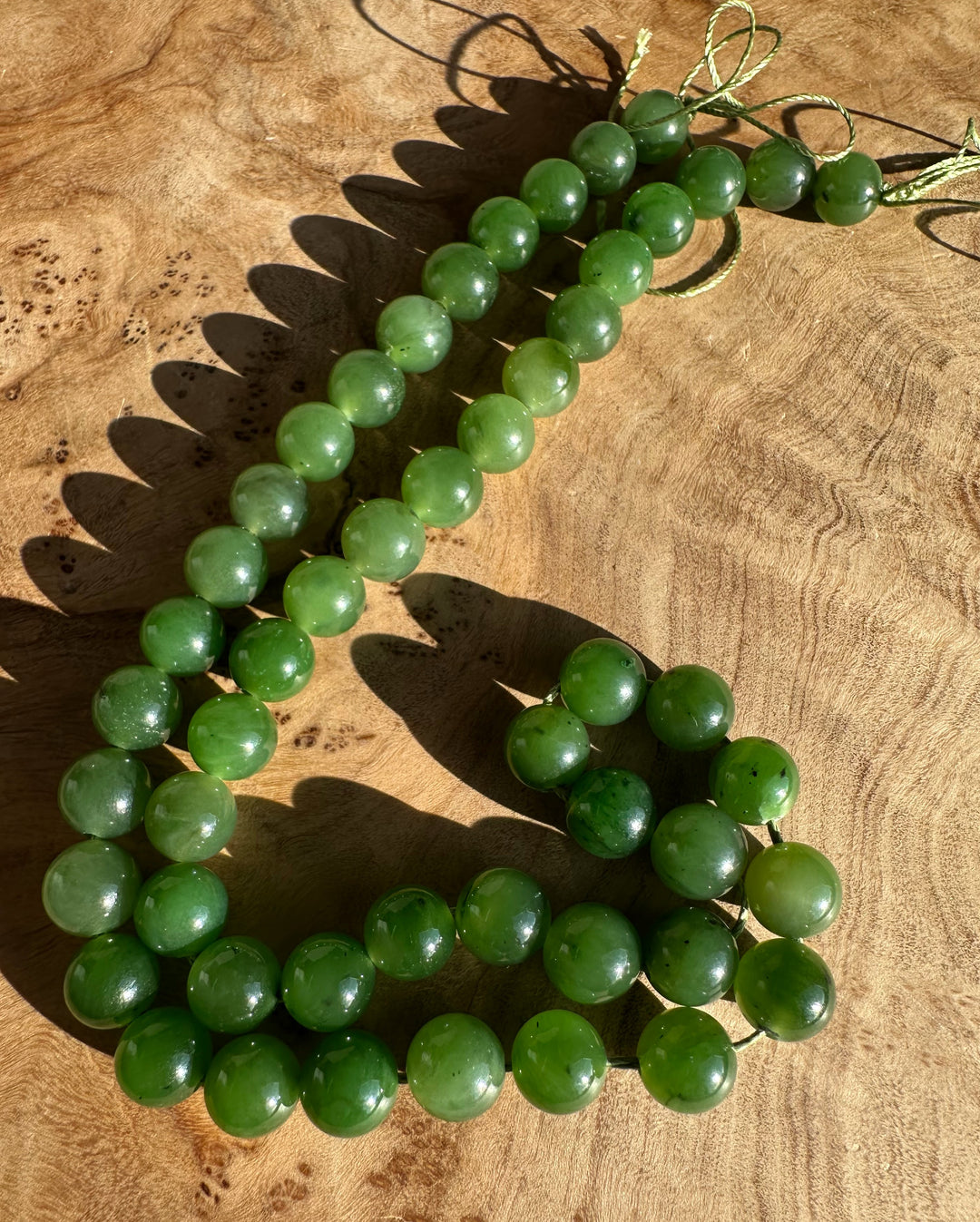 Green 8mm Canadian beads on a string laid on wood in a curved strand