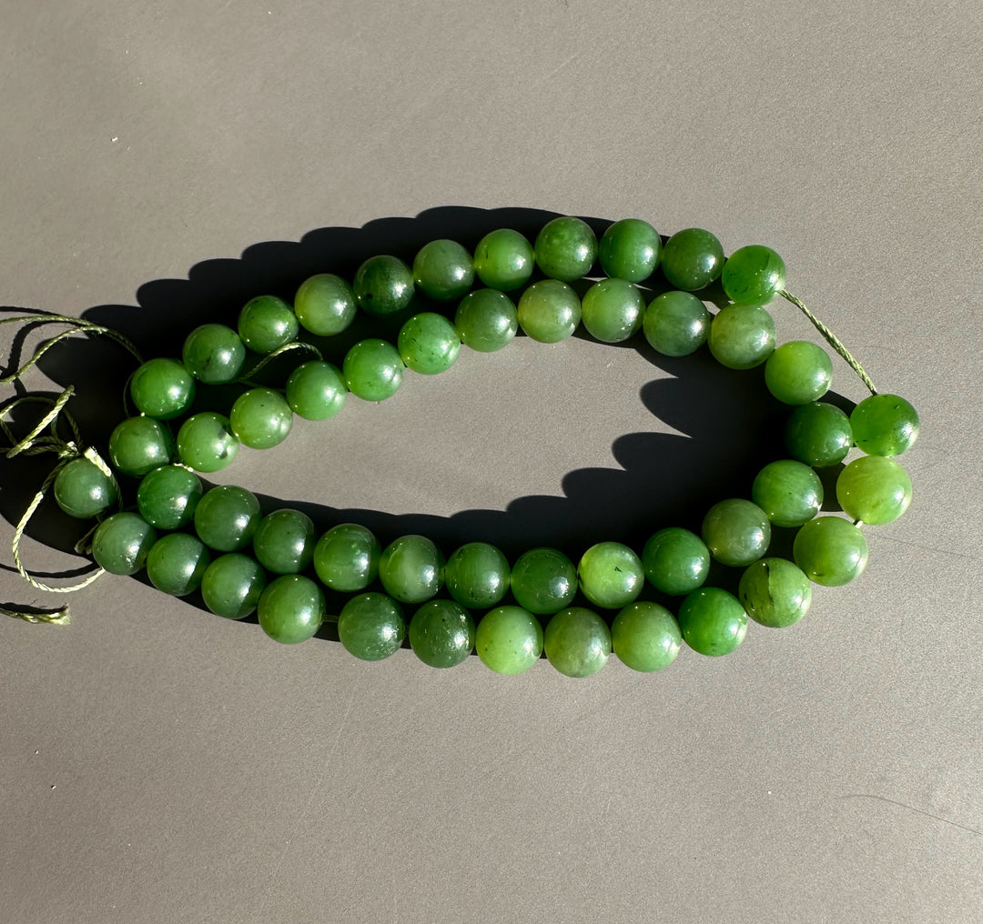 Shiny green 8mm unstrung Canadian beads arranged in a coil on a gray surface with visible twine ends