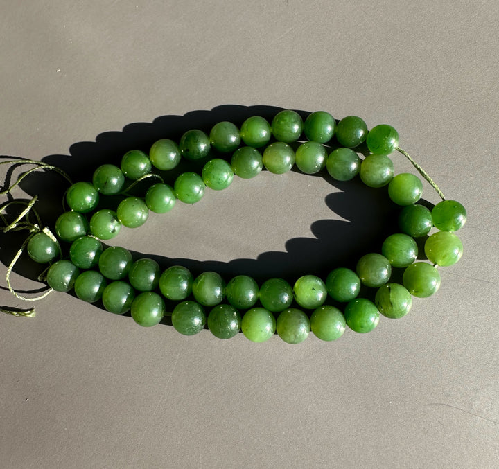 Shiny green 8mm unstrung Canadian beads arranged in a coil on a gray surface with visible twine ends