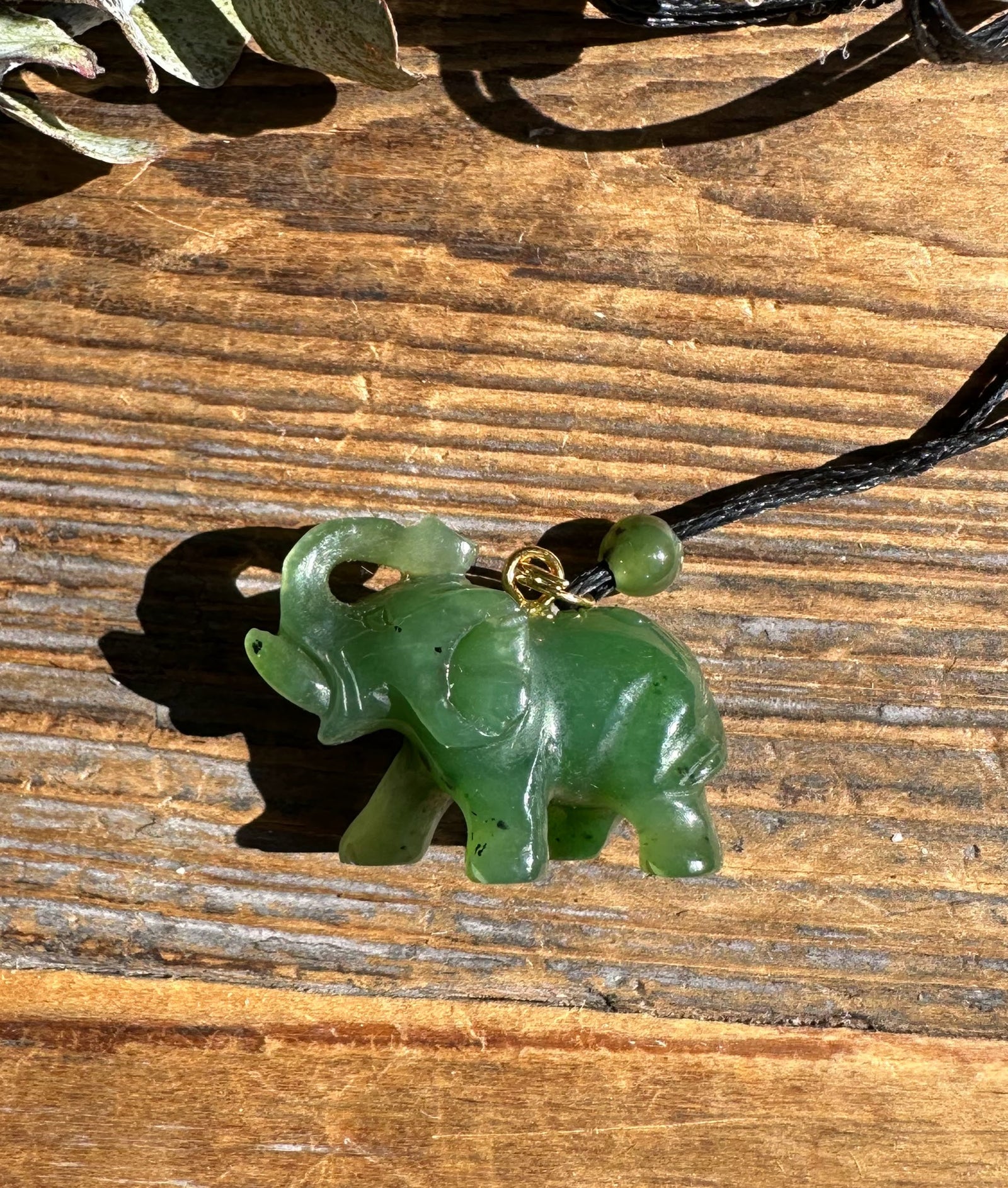 Jade elephant pendant with a green bead on a black cord against a wooden surface