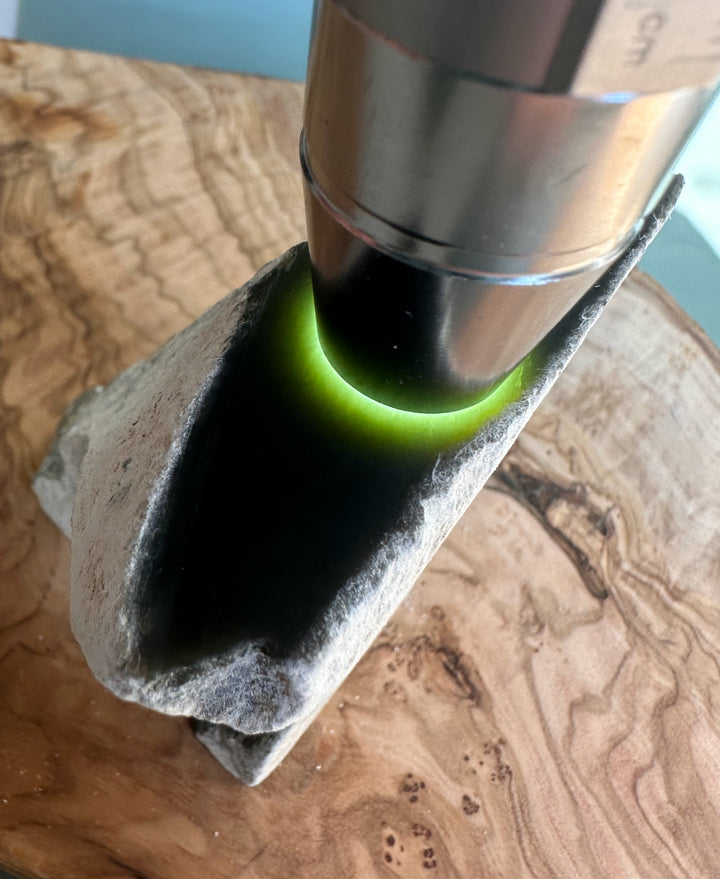 Wyoming Honey Olive Jade specimen with a metal cylinder entering a hollow rock and a green glow around the rim.
