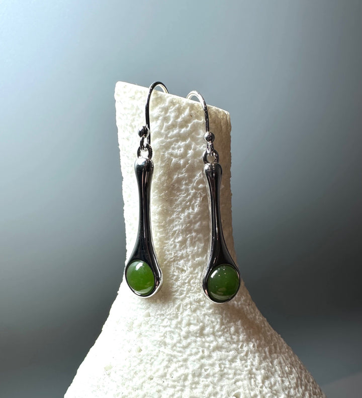 Close up of silver drop earrings with green stones hanging from a curved hook on a display stand.