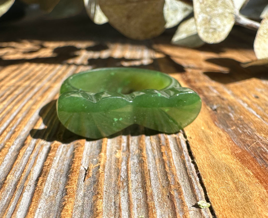Green jade hearts band ring with heart shaped edge resting on a weathered wooden surface.