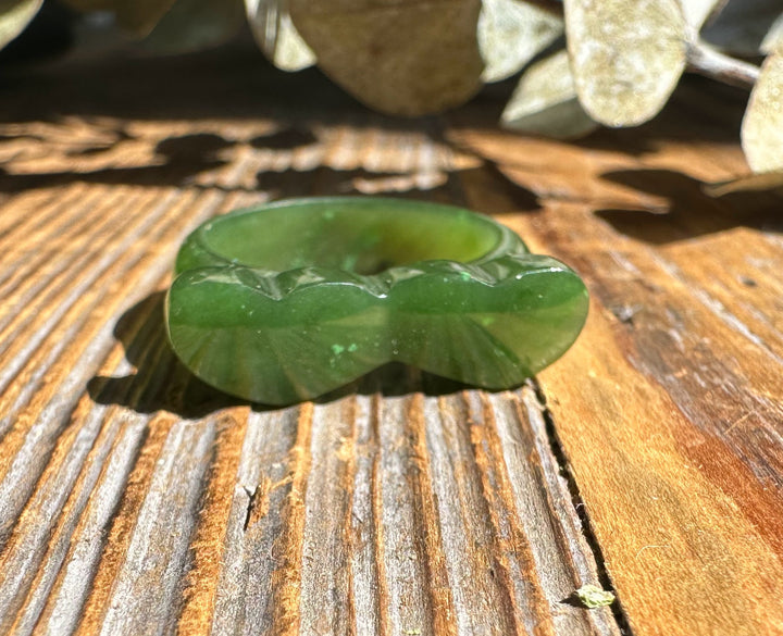 Green jade hearts band ring with heart shaped edge resting on a weathered wooden surface.