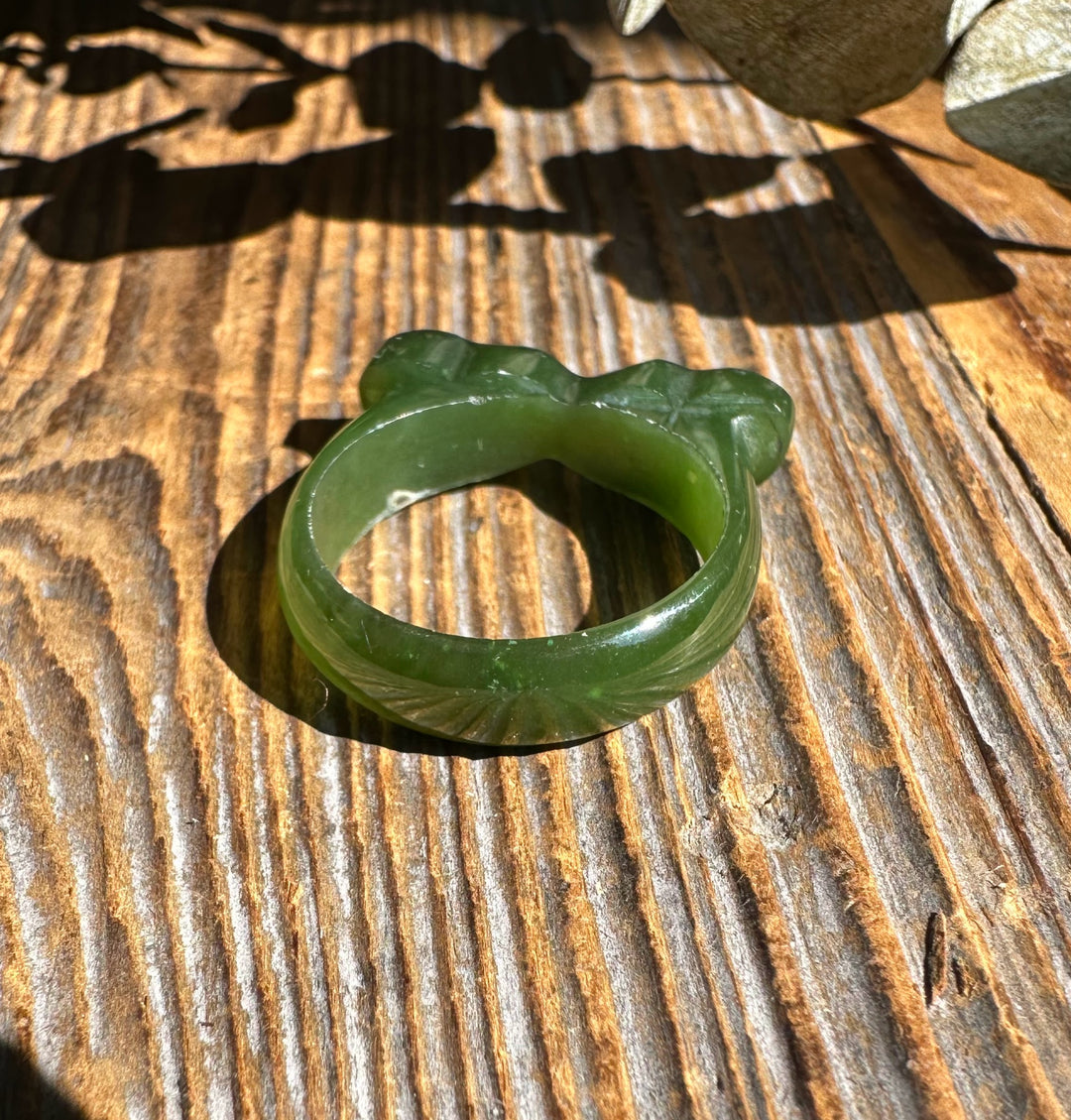 Canadian Jade Hearts Band Ring in green jade with heart motifs on a rustic wooden surface