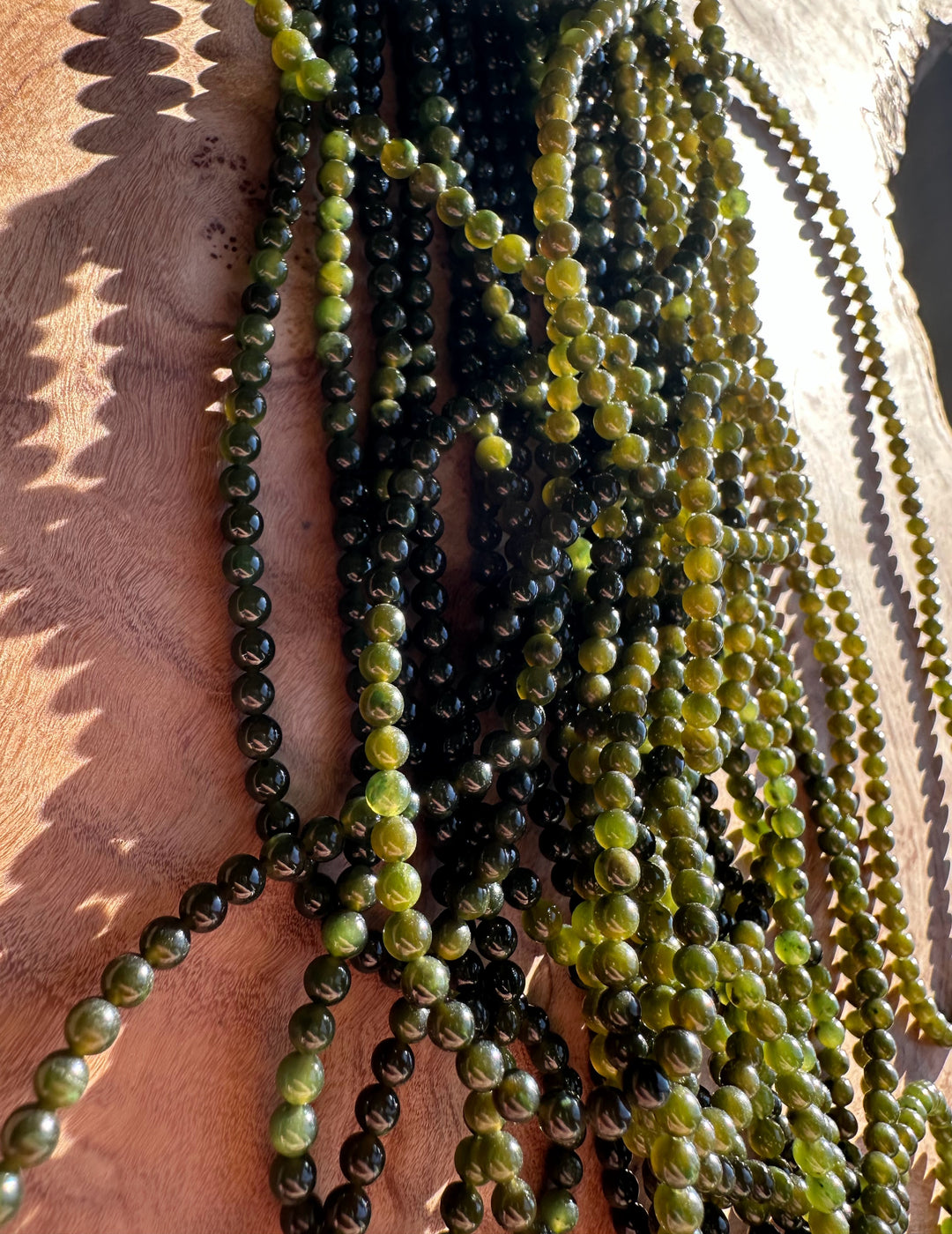 Several strands of green nephrite jade beads draped over a person showing color variation and length.