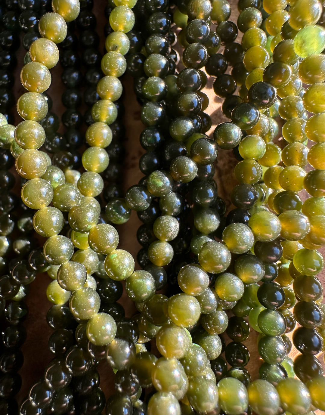 Close-up of glossy nephrite jade beads in varying dark to light green and yellow hues.