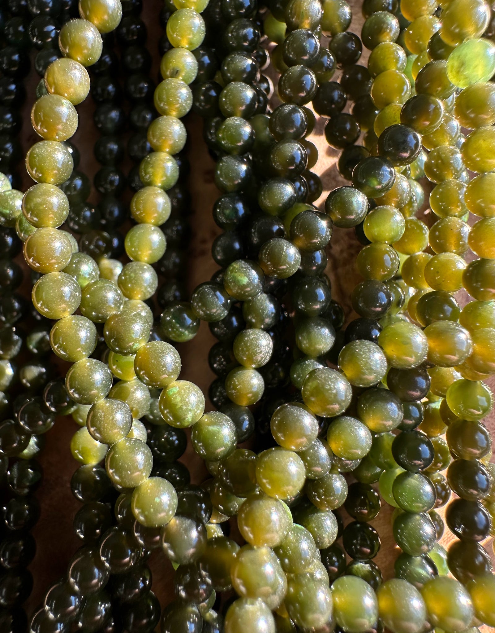 Close-up of glossy nephrite jade beads in varying dark to light green and yellow hues.