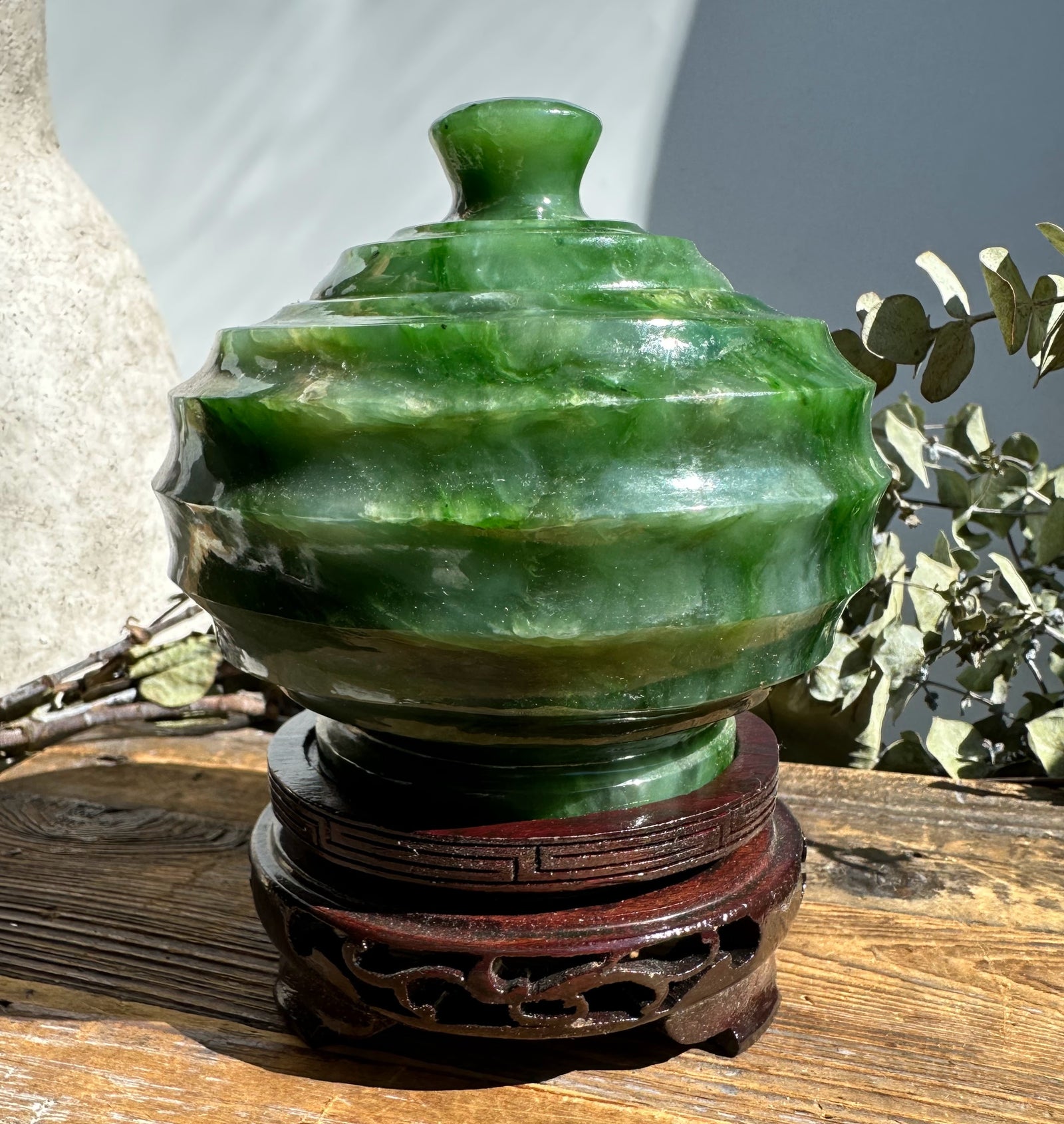 Polar Jade Pot with lid on a carved wooden stand in sunlight