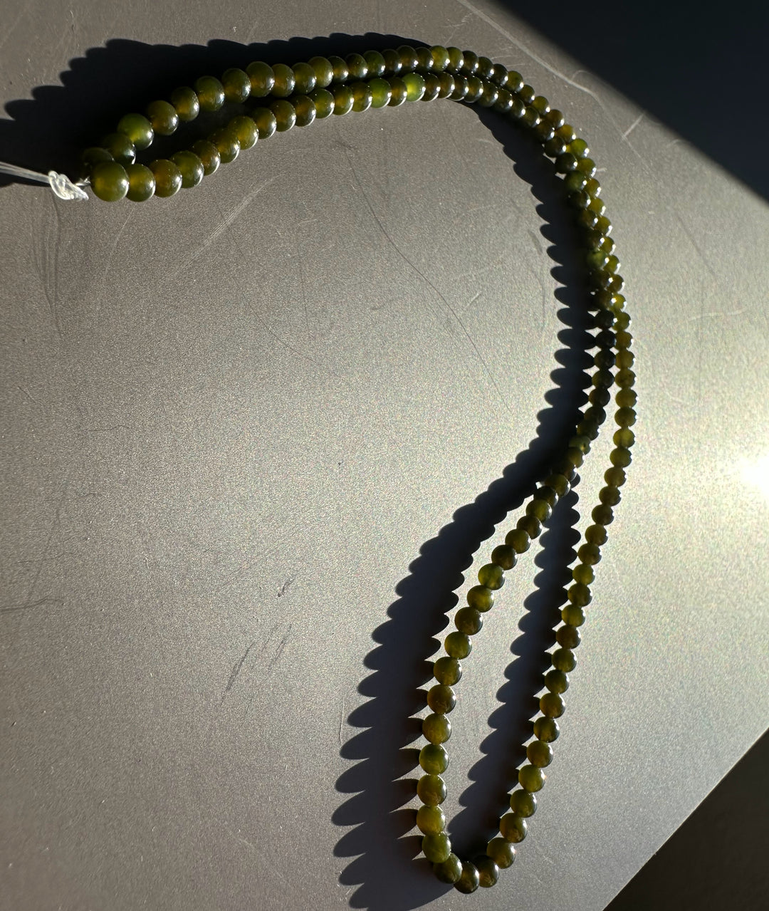 Dark green 3mm nephrite jade beads arranged in a loop on a gray surface