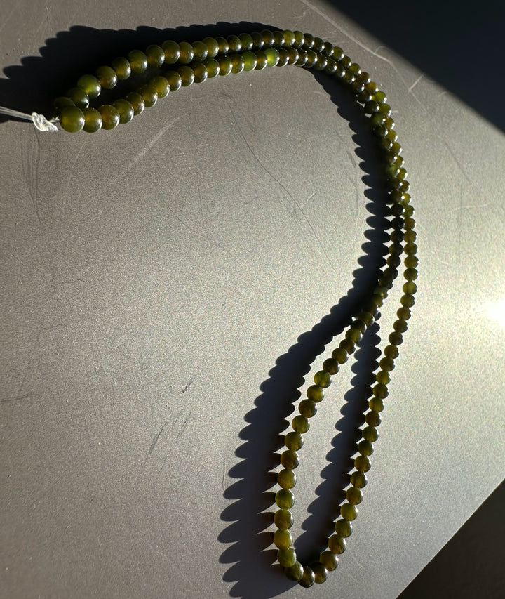Dark green 3mm nephrite jade beads arranged in a loop on a gray surface