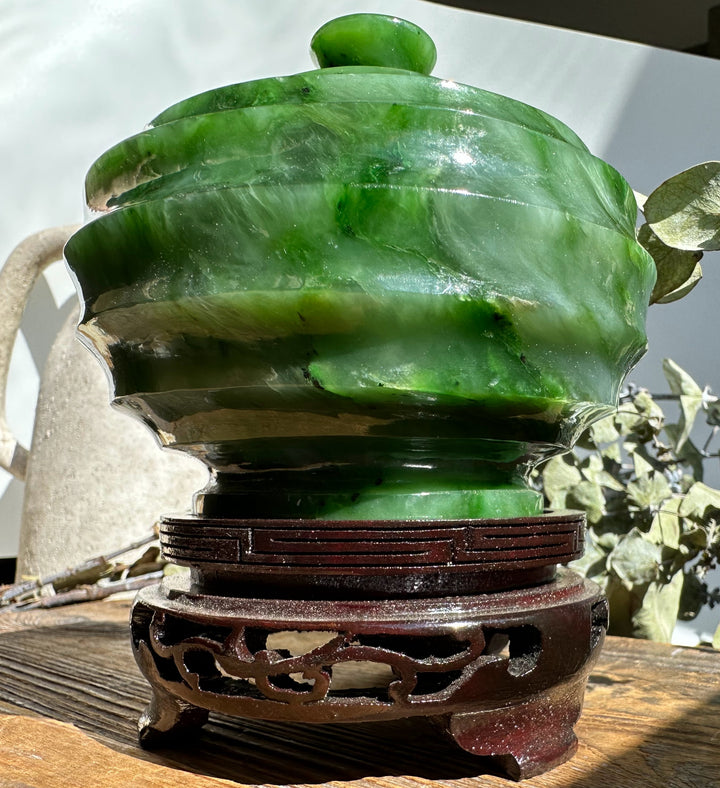 Polar Jade Pot with lid on a carved dark wooden stand outdoors, featuring glossy layered green jade.