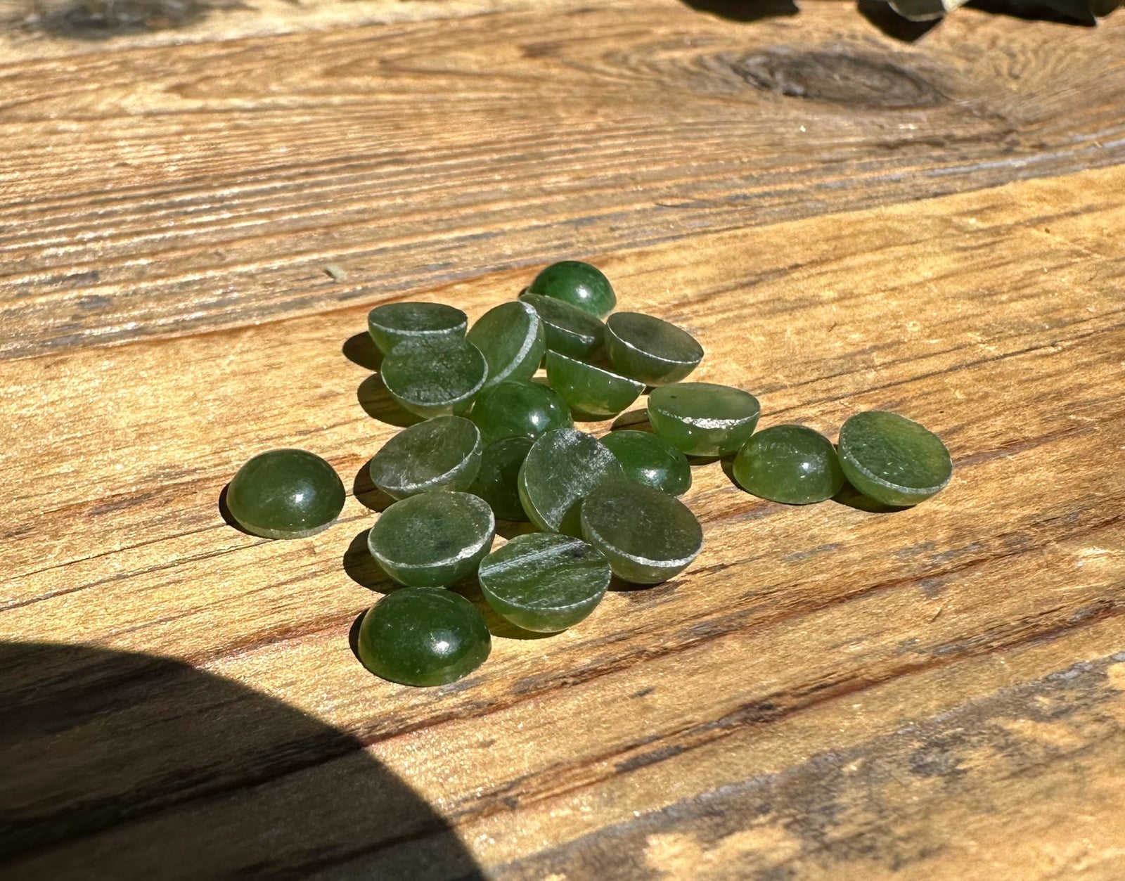 Assorted 7mm round nephrite jade cabochons spread on a wooden surface