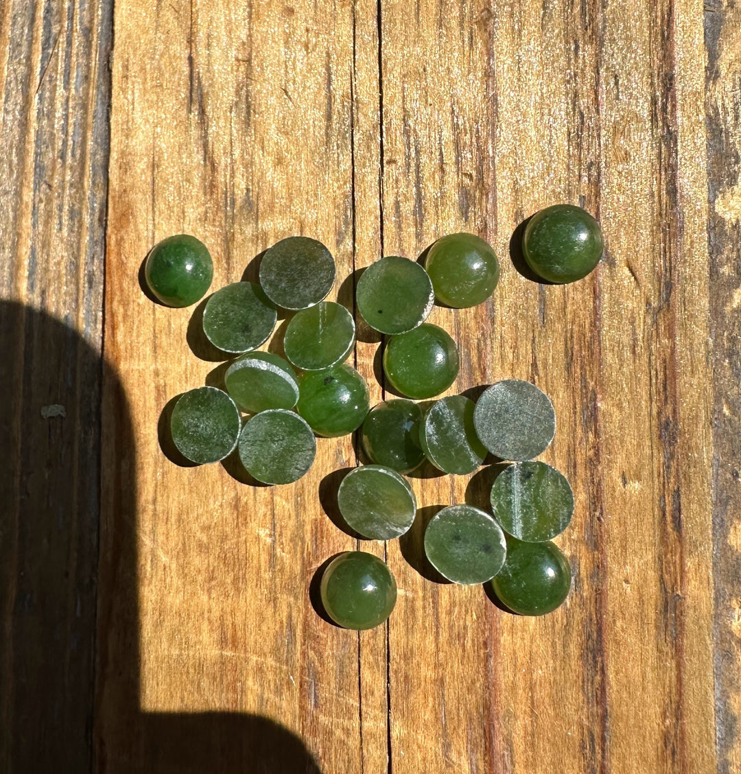 Twenty 7mm round nephrite jade cabochons scattered on a wooden surface.