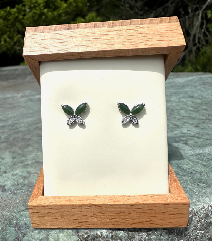 Silver butterfly stud earrings with green enamel wings and clear crystal accents on a cream display inside an open wooden box
