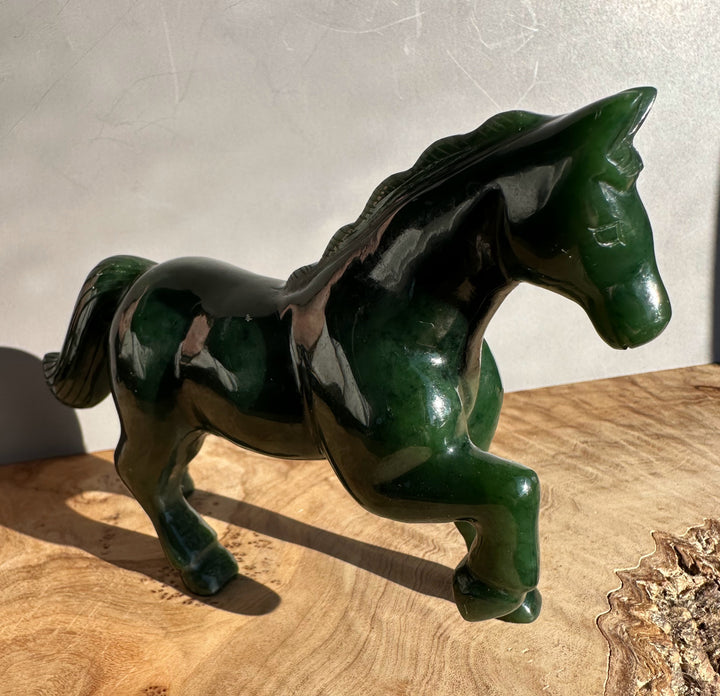 Three-quarter view of a glossy dark green nephrite jade horse sculpture five inches long.