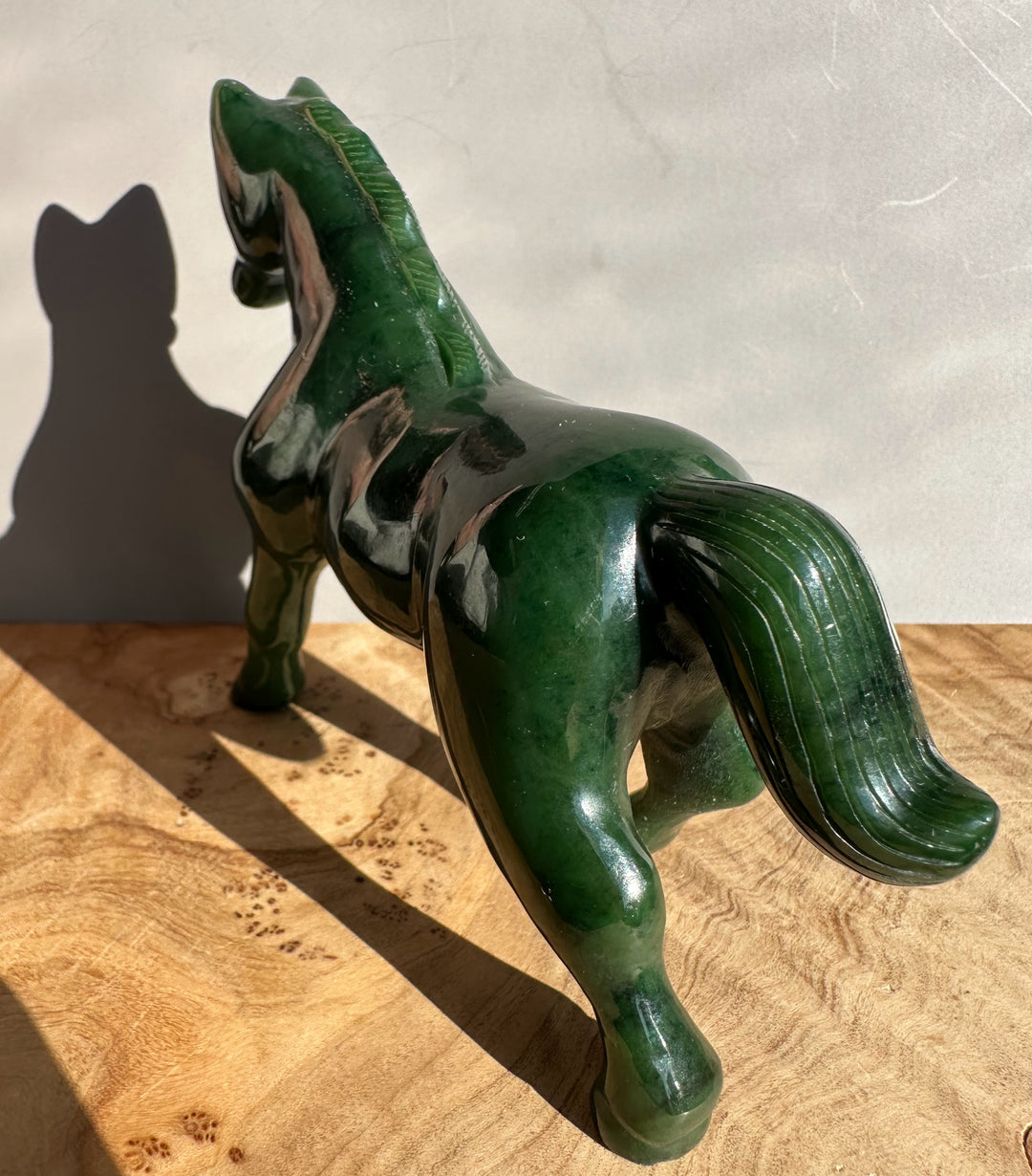 Dark green nephrite jade horse statue shown in side profile with one foreleg raised and a polished surface