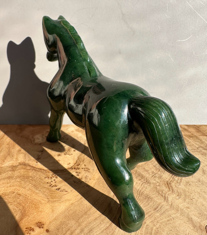 Dark green nephrite jade horse statue shown in side profile with one foreleg raised and a polished surface