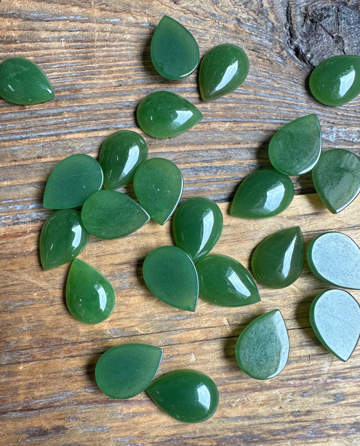 Glossy green pear shaped cabochons scattered on a rustic wooden surface