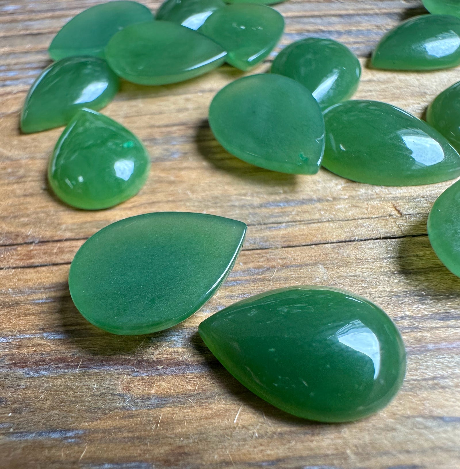 Polished green pear teardrop cabochons 10x14mm scattered on a wooden surface