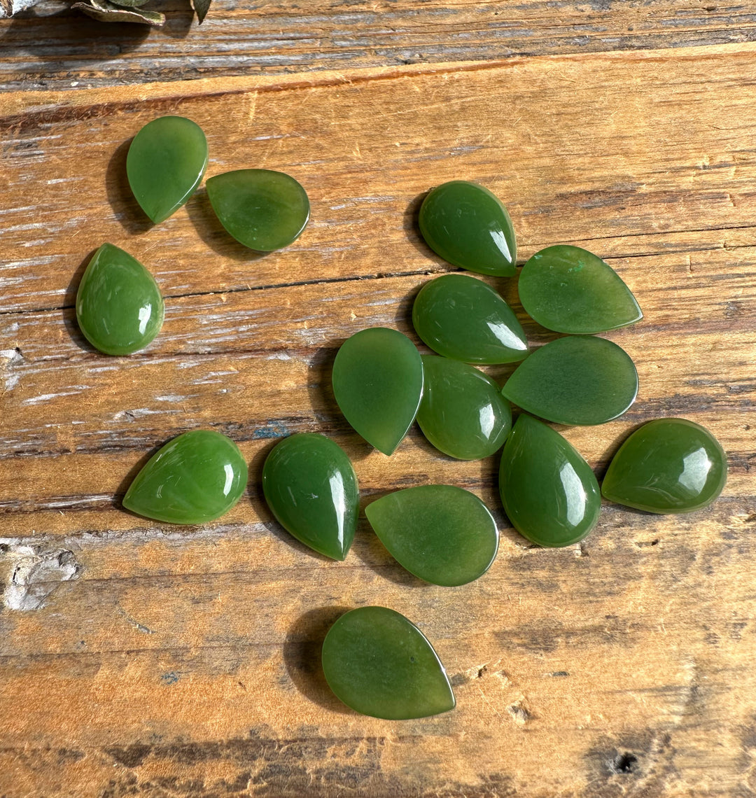 Green teardrop cabochons arranged on a rustic wooden table