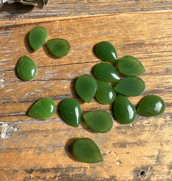 Green teardrop cabochons arranged on a rustic wooden table