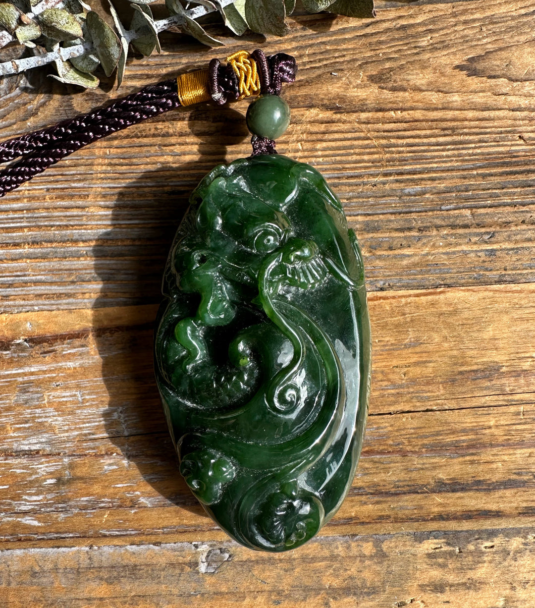 Green jade dragon pocket pendant with swirling carved dragon motifs, hung on a dark brown braided cord with a green bead.