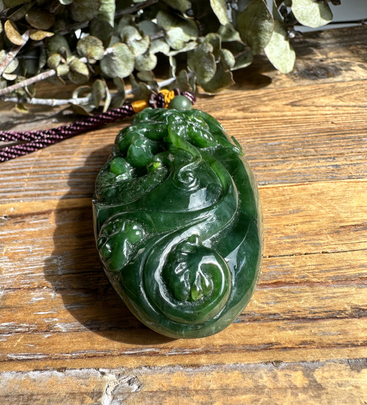 Dragon pocket pendant carved from deep green jade resting on a rustic wooden surface with a braided cord.