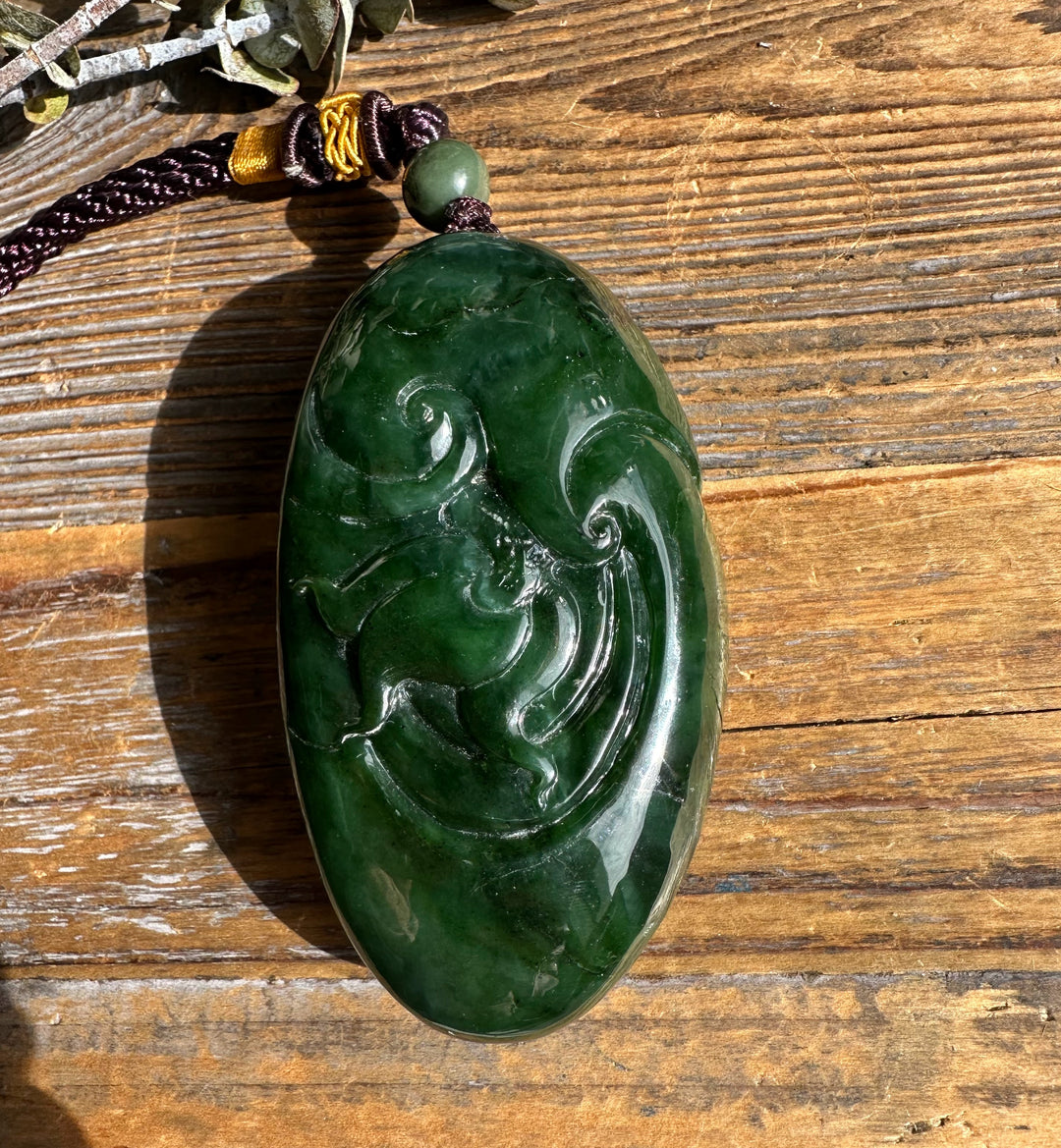 Top view of a green jade dragon pocket pendant attached to a braided cord with bead showing carved details.