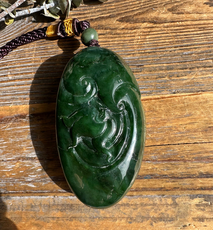 Top view of a green jade dragon pocket pendant attached to a braided cord with bead showing carved details.