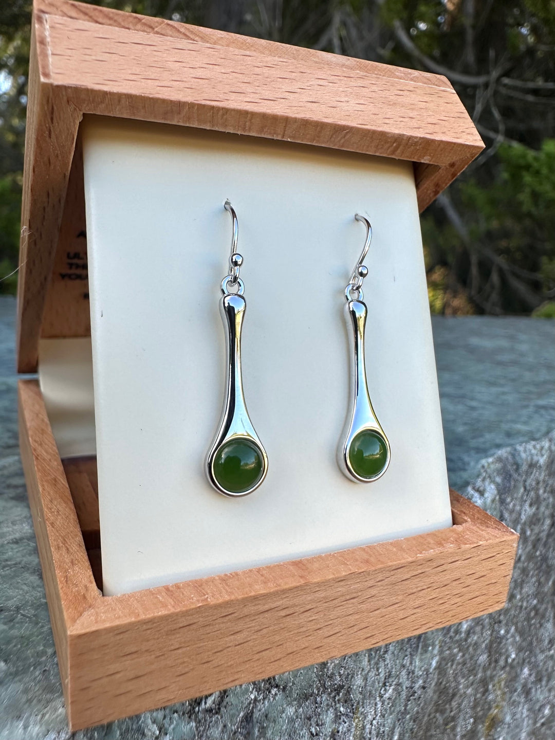 Silver drop earrings with green cabochon stones displayed in a wooden jewelry box.