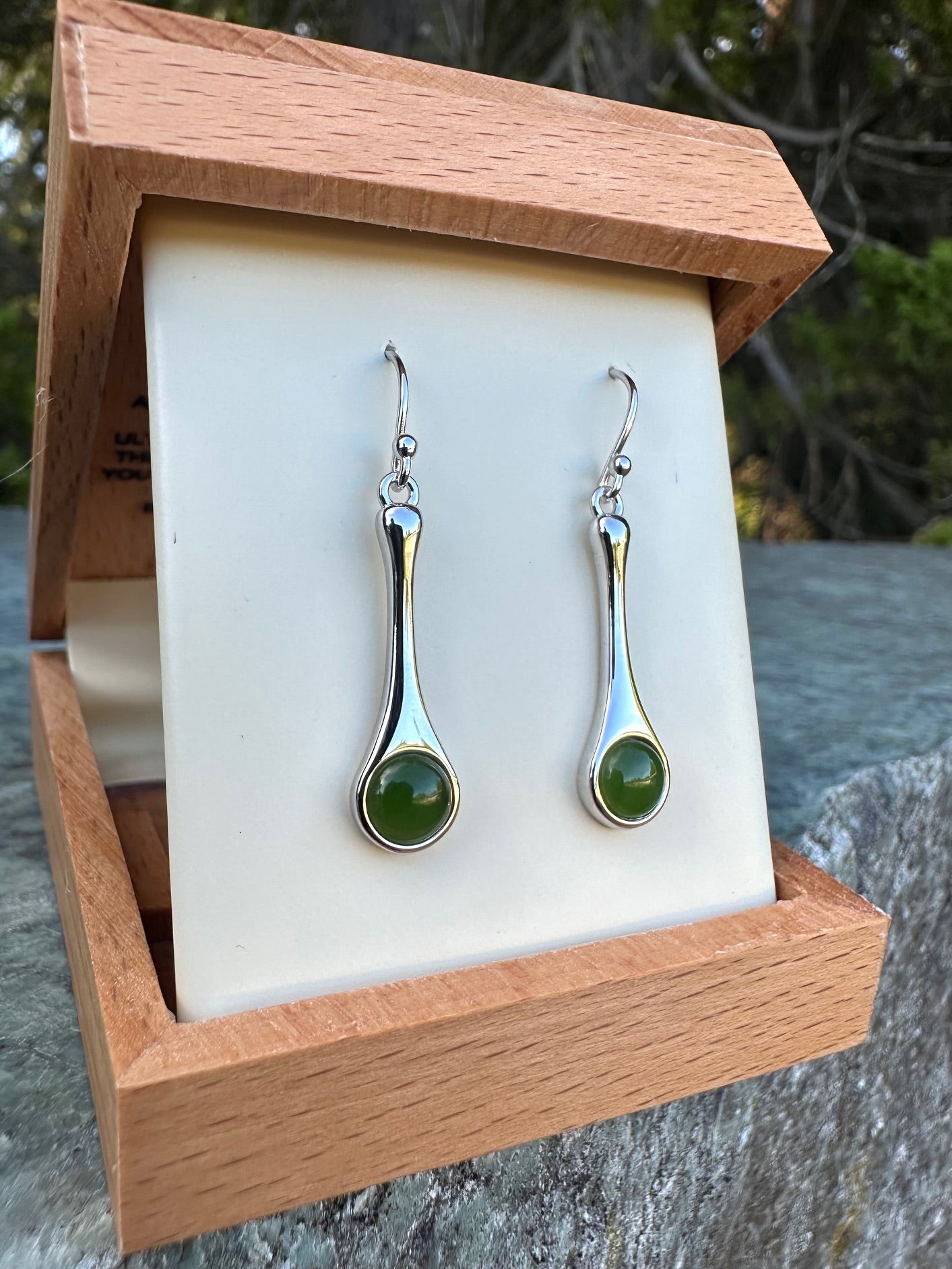 Silver drop earrings with green cabochon stones displayed in a wooden jewelry box.