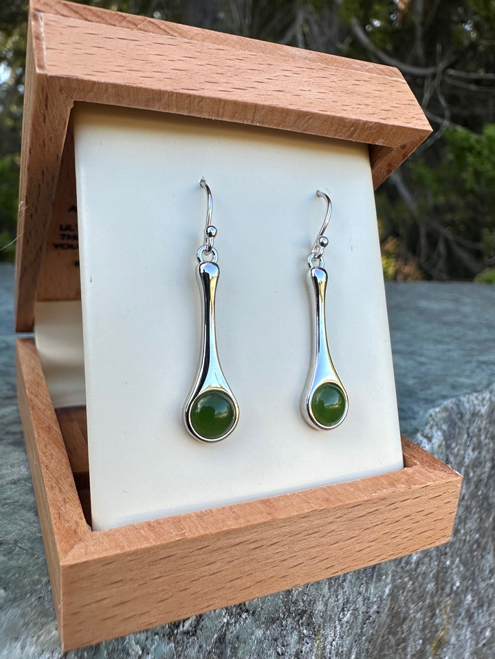 Silver drop earrings with green cabochon stones displayed in a wooden jewelry box.