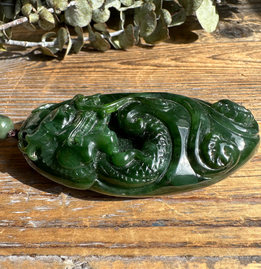 Side view of green jade dragon pocket pendant with swirling carved patterns and glossy finish.