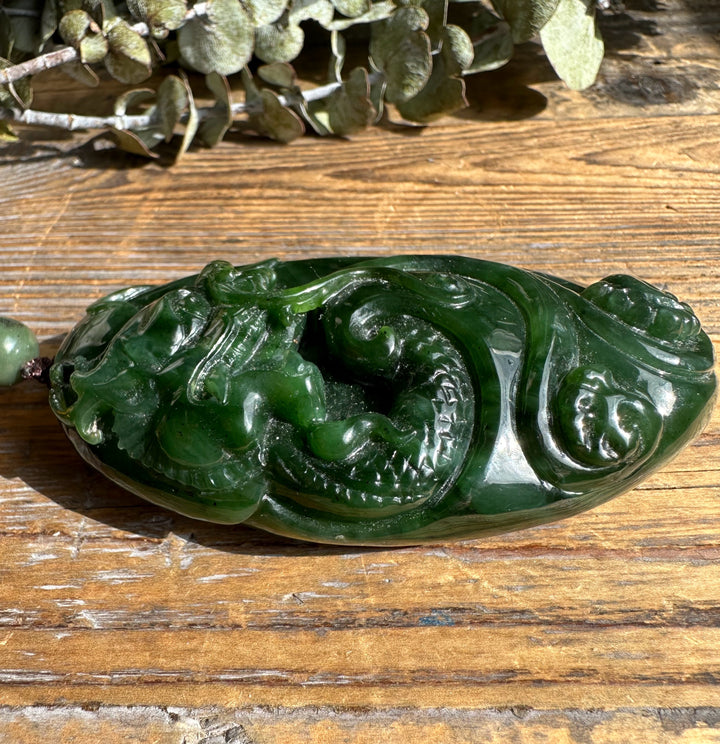 Side view of green jade dragon pocket pendant with swirling carved patterns and glossy finish.