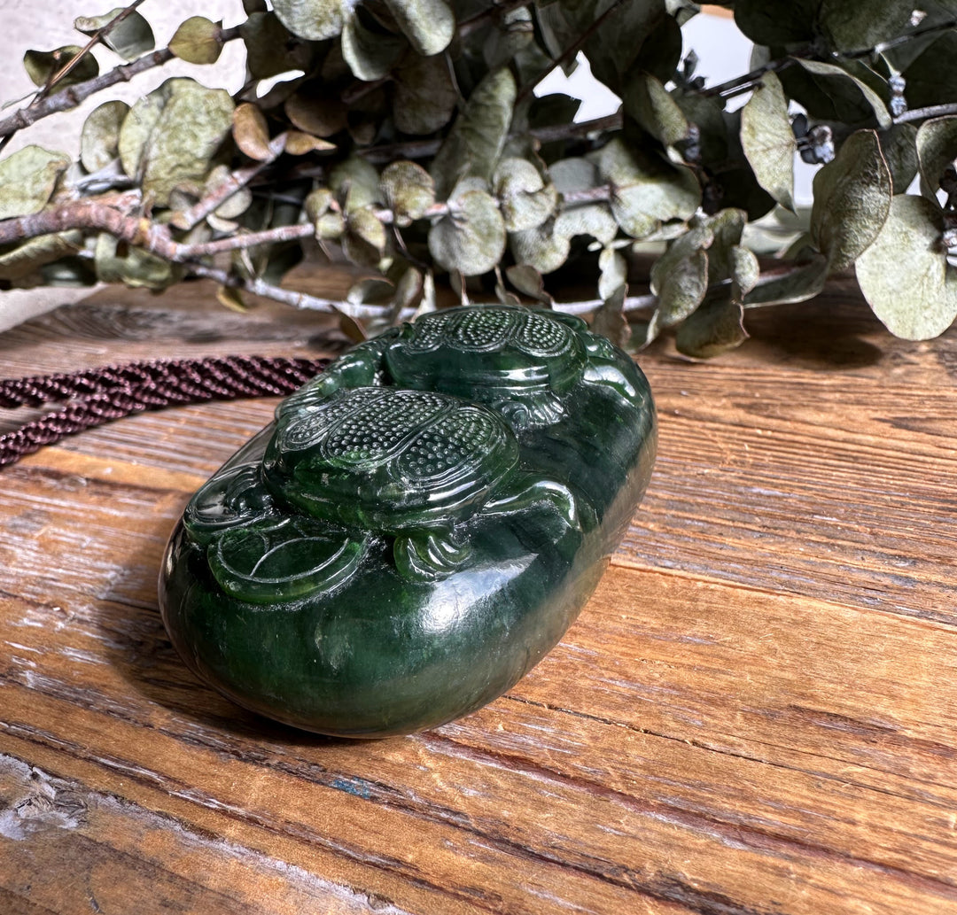 Close-up of the glossy dark green jade pendant featuring twin turtle reliefs on a wooden surface