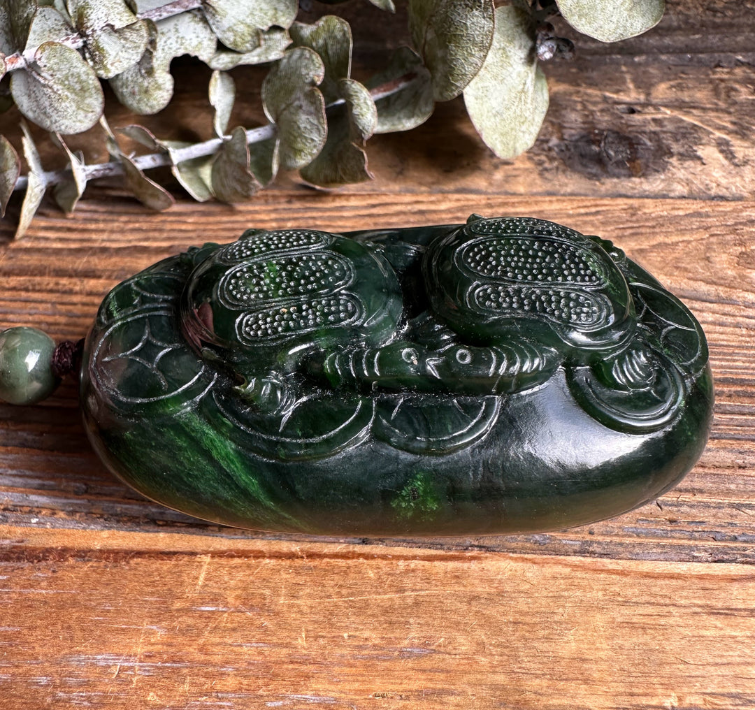 Top angled view of the two turtle jade pendant with cord and bead on a rustic wooden table