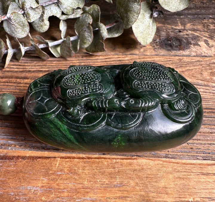 Top angled view of the two turtle jade pendant with cord and bead on a rustic wooden table