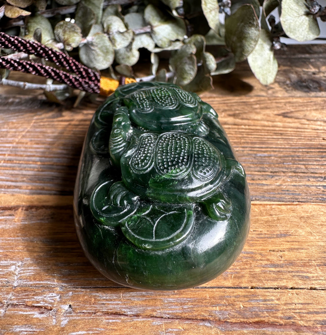 Glossy dark green Canadian jade pendant carved with two turtles on a cord.